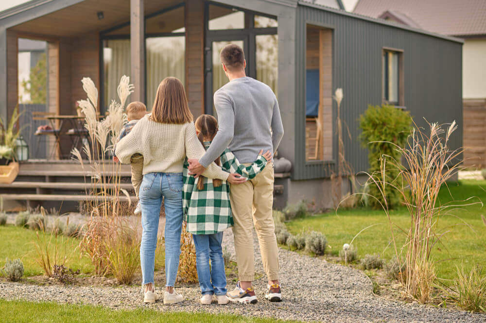 Eine vierköpfige Familie steht gemeinsam draußen und blickt auf ihr modernes Haus an einem sonnigen Tag