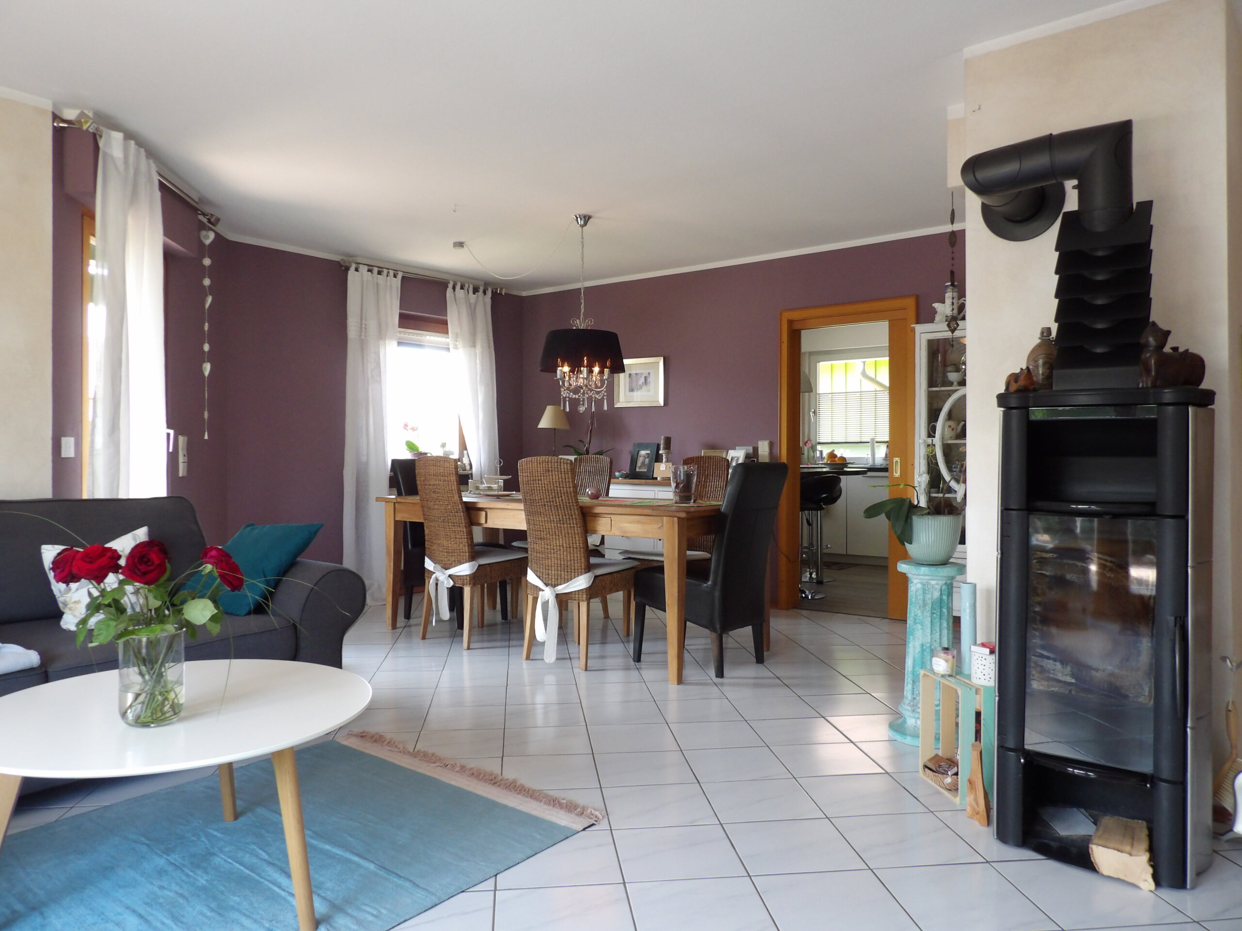 Modernes Wohn- und Esszimmer in einem Neuried Einfamilienhaus mit lila Wänden, Holzofen, großen Fenstern und hellem Couchtisch