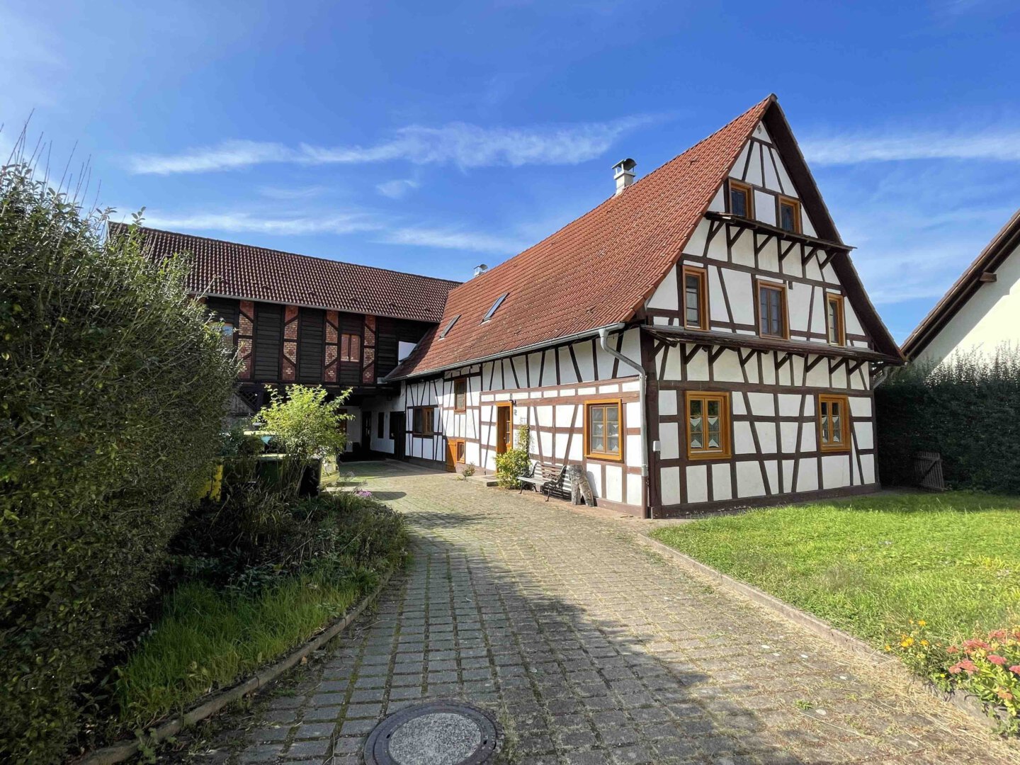 Traditionelles Zweifamilienhaus im Fachwerkstil mit rotem Dach, weißen Wänden und Kopfsteinpflaster-Einfahrt unter blauem Himmel