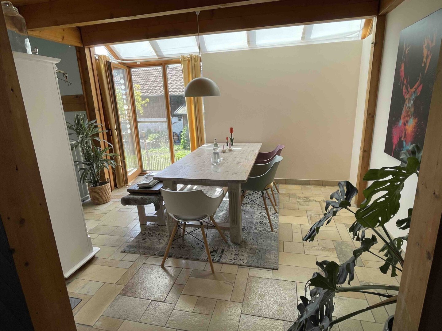 Heller Essbereich im Schwanau Architektenhaus mit Holztisch, verschiedenen Stühlen, Pflanzen, großen Fenstern und farbenfroher Kunst