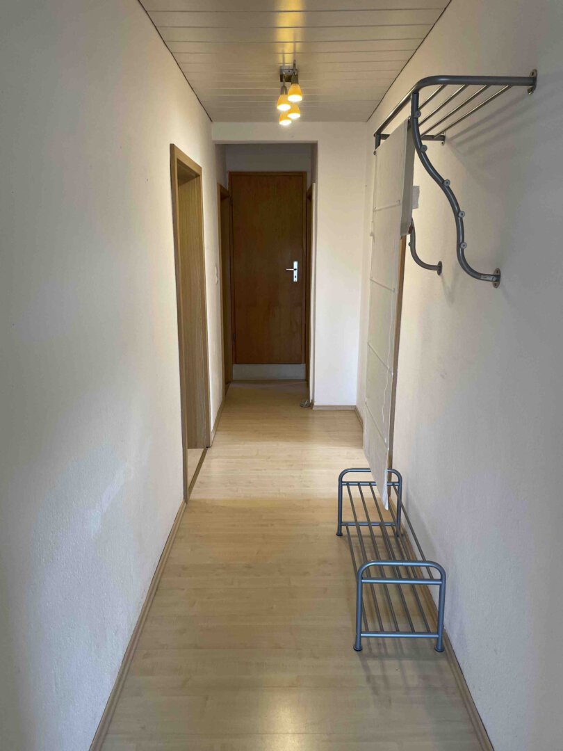 Schmaler Flur mit hellem Holzboden, Metallgarderoben und brauner Tür, ideal für ein Dreifamilienhaus oder Kapitalanleger