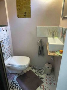 Kleines Bad im Schwanau Architektenhaus mit Wand-WC, gemusterten Fliesen, Holzbordwaschbecken und brauner Badematte