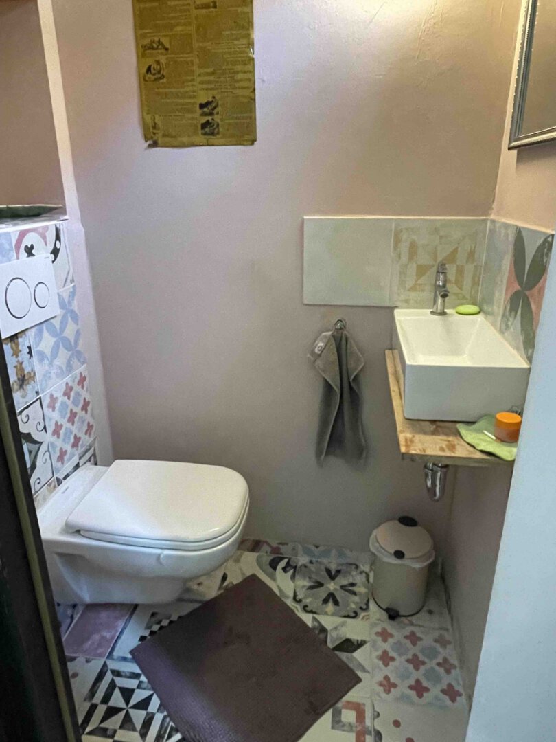 Kleines Bad im Schwanau Architektenhaus mit Wand-WC, gemusterten Fliesen, Holzbordwaschbecken und brauner Badematte