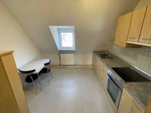 Gemütliche Dachgeschossküche im Dreifamilienhaus mit Holzmöbeln, Herd, Spüle und einem Zweiertisch unter der Dachschräge