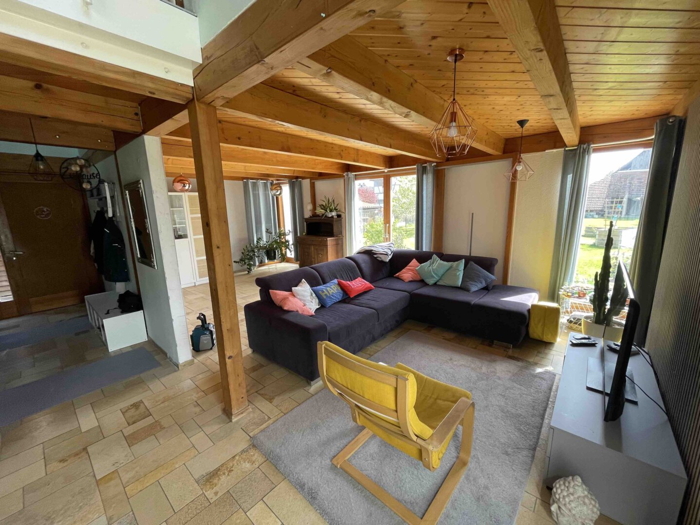 Gemütliches Wohnzimmer in einem modernen Architektenhaus mit Ecksofa, bunten Kissen, gelbem Sessel, Fernseher und viel Tageslicht