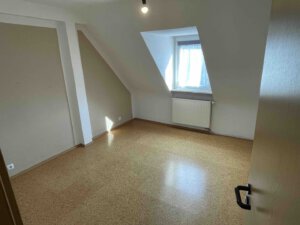 Leeres Zimmer mit schräger Decke, Korkboden und Fenster, geeignet für Dreifamilienhaus oder Kapitalanleger