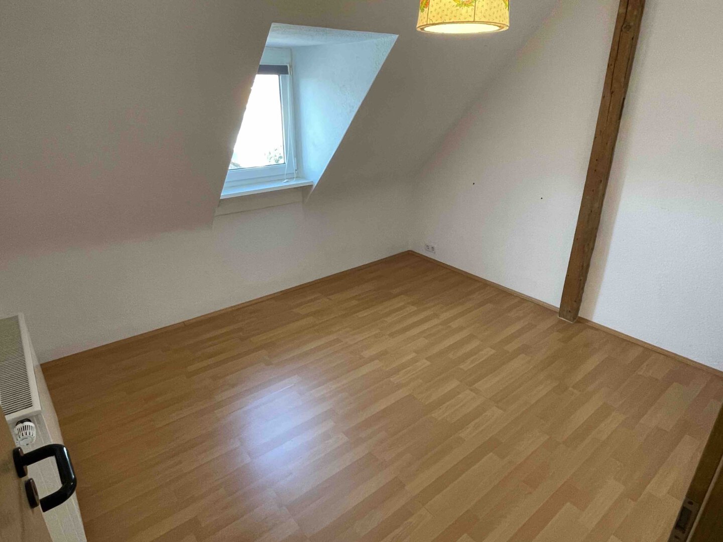 Helles Dachgeschosszimmer mit schräger Decke, sichtbarem Balken und Laminatboden, ideal für Kapitalanleger in einem Dreifamilienhaus