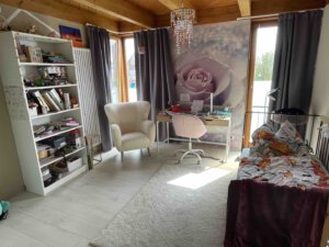 Gemütliches Schlafzimmer in einer Doppelhaushälfte mit Schreibtisch, Sessel, Bücherregal, Tagesbett und großer Rosenwand, von Tageslicht erhellt