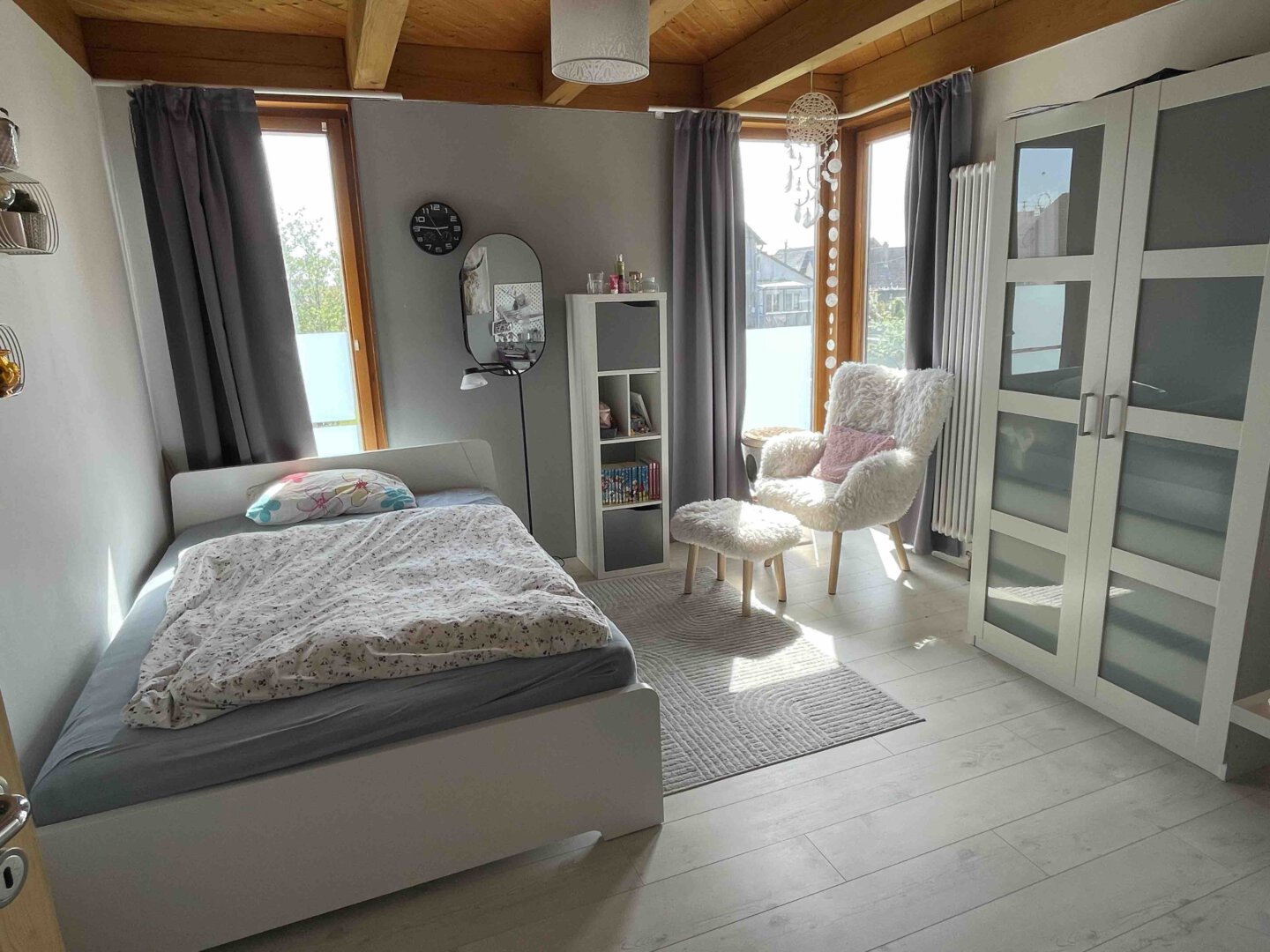 Gemütliches Schlafzimmer in einer Doppelhaushälfte in Schwanau mit Bett, Sessel, Hocker, Kleiderschrank, Regalen und großen Fenstern