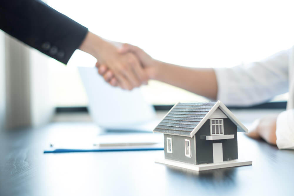 Zwei Personen geben sich nach der Immobilienbewertung im Büro die Hand; auf dem Tisch steht ein Modellhaus für den Notartermin